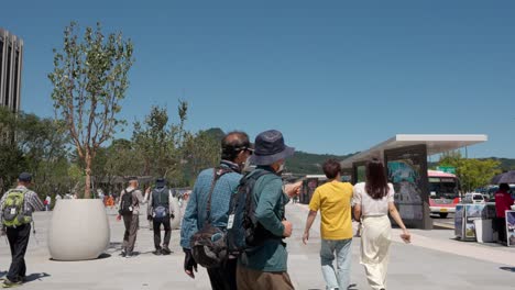 Senior-Korean-travelers-walking-in-face-masks-at-renovated-Gwanghwamun-Plaza-in-downtown-Seoul---copy-space,-establishing-shot