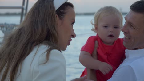 Mom-telling-the-father-a-funny-story-while-dad-has-his-hands-full-with-their-child,-on-a-sailboat-in-the-Mediterranean