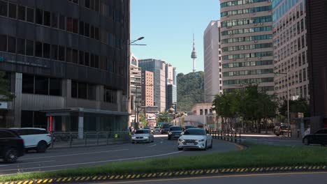 Busy-traffic-turning-in-city-center-with-many-cars-and-view-of-N-Seoul-Tower-from-downtown-city-streets-with-skyscrapers