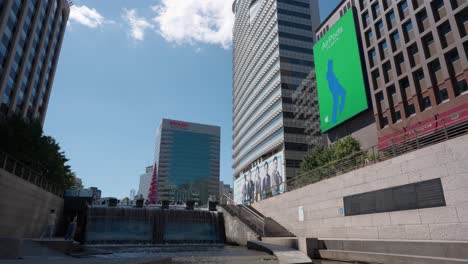 Enorme-Pantalla-De-Pared-Digital-De-Publicidad-Pública-Reproduciendo-Airpods-Comercial-Cerca-Del-Parque-Del-Arroyo-Cheonggyecheon-En-Un-Hermoso-Día-De-Verano-En-La-Ciudad-De-Seúl,-Corea-Del-Sur