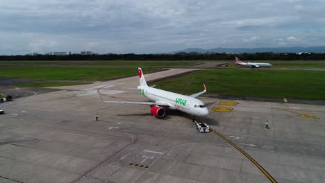 Luftaufnahme-Eines-Fahrzeugs,-Das-Ein-Flugzeug-Auf-Einem-Sonnigen-Flughafen-Zur-Landebahn-Schiebt