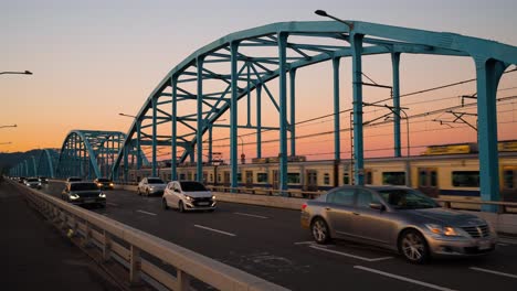 Dongjak-brücke-Gegen-Einen-Sonnenuntergangshimmel-Mit-Seoul-u-bahnzug,-Der-Von-Der-U-bahnstation-Dongjak-Fährt,-Und-Vielen-Autos-Auf-Der-Stadtautobahn,-Südkorea