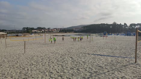 Ein-Erwachsener-Beach-soccer-trainer-Mit-Kindern-Beobachtet-An-Einem-Sommermorgen-In-Bunten-T-shirts-Das-Geschäft-Zwischen-Den-Volleyballnetzen,-Rollender-Schuss-Nach-Rechts