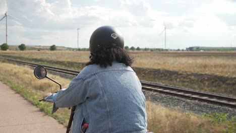 Woman-with-jeans-jacket-on-driving-slowly-on-a-bicycle-road-with-an-electric-scooter