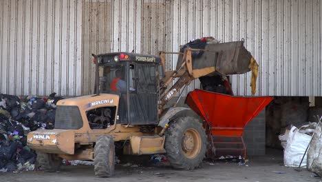 Una-Excavadora-Arroja-Basura-En-Una-Cinta-Transportadora-Dentro-De-Una-Instalación-De-Procesamiento-De-Residuos