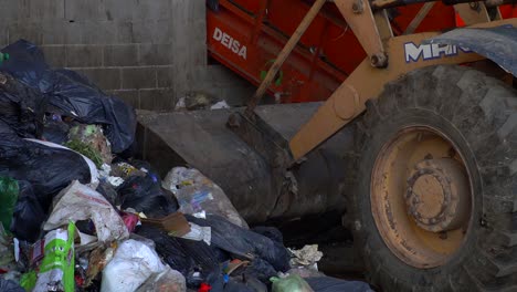 A-bulldozer-loads-the-bucket-with-waste-for-further-dumping-onto-a-conveyor-belt-inside-a-waste-processing-facility