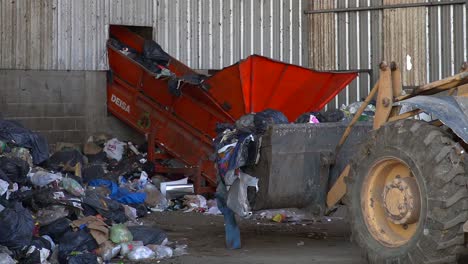 Una-Excavadora-Se-Acerca-A-Una-Cinta-Transportadora-Para-Arrojar-Basura-Dentro-De-Una-Planta-De-Procesamiento-De-Desechos