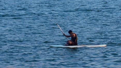 Niño-Hispano-Sentado-En-Una-Tabla-De-Surf-Y-Remando-En-El-Lago-Paranoa