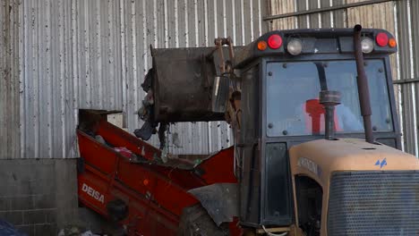 Back-view-of-a-bulldozer-as-it-dumps-waste-onto-a-conveyor-belt-inside-a-waste-processing-facility