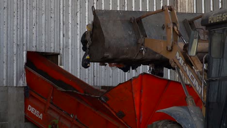 Back-view-of-a-bulldozer's-bucket-dumping-waste-onto-a-conveyor-belt-inside-a-waste-processing-facility