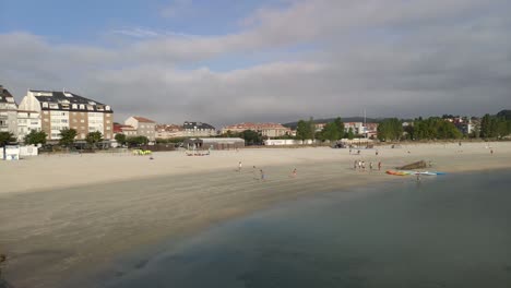 Personas-Y-Niños-Realizan-Actividades-Deportivas-De-Ocio-En-Grupos-En-La-Arena-De-La-Orilla-De-La-Playa-En-Una-Mañana-Nublada,-Tiro-Panorámico-Bloqueado,-Porto-novo,-Galicia,-España