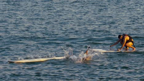 Frau,-Die-Während-Der-Goldenen-Stunde-Vom-Sup-Board-Ins-Wasser-Fällt,-Zeitlupe