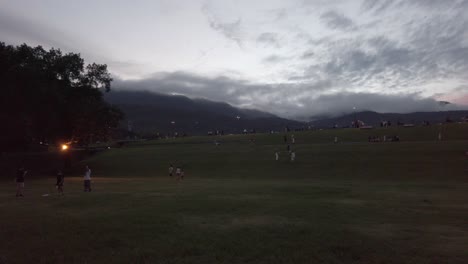 Paisaje-De-Campo-De-Hierba-Verde-Con-Mucha-Gente-Disfrutando-De-Actividades-Al-Aire-Libre-Al-Atardecer