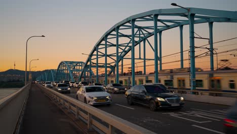 Dos-Trenes-Del-Metro-De-Seúl-Van-En-Direcciones-Opuestas-En-El-Puente-Dongjak-Al-Atardecer,-Y-Muchos-Autos-Están-En-Tránsito-En-La-Carretera-Del-Puente,-Corea-Del-Sur