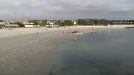 Dos-Niños-Jugando-Fútbol-Y-Un-Grupo-De-Adolescentes-Entrenan-Para-Practicar-Remo-En-Canoa-Una-Mañana-Nublada,-Tiro-Panorámico-Bloqueado,-Porto-novo,-Galicia,-España