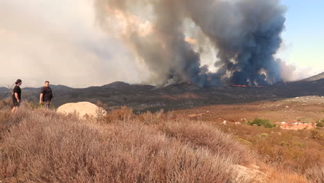 Dos-Personas-En-La-Cima-De-Una-Montaña-Miran-Un-Incendio-Forestal-Y-Toman-Fotos