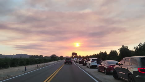 Toma-Pov-De-Un-Vehículo-De-Motor-Que-Conduce-A-Lo-Largo-De-Una-Carretera-Congestionada,-El-Arcén-De-La-Carretera-Bordeado-De-Vehículos-Estacionados-Mientras-La-Gente-Ve-La-Devastación-Causada-Por-El-Incendio-De-Fairview-Al-Atardecer,-Hemet,-California