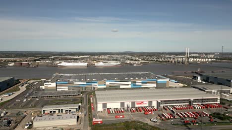 Drohnenansicht-Des-Industriegebiets-In-Dartford-Mit-Blick-Auf-Die-Amazon--Und-Europa-Lagerhäuser-Und-Die-Königin-Elizabeth-II-Brücke-über-Den-Fluss-Und-Handelsschiffe-Im-Hintergrund