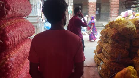 Pov-Caminando-Detrás-De-Un-Comerciante-Pasando-Montones-De-Sacos-De-Cebolla-Apilados-En-Un-Almacén-En-Bangladesh