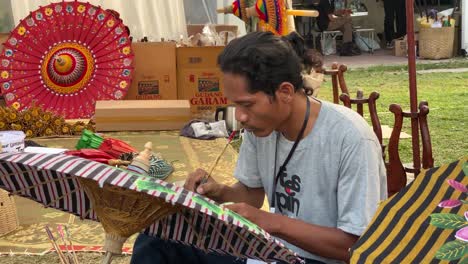 Umbrella-painting-artist,-who-is-painting-his-work-at-the-Indonesian-Umbrella-Festival