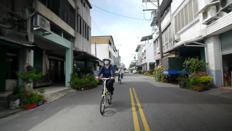 Front-on-view-of-Asian-woman-in-face-mask-riding-through-well-developed-village-during-day-time