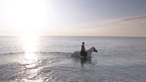 Mujer-Con-Casco-Montando-A-Caballo-Dentro-Del-Agua-Del-Océano-Al-Atardecer,-Cámara-Lenta