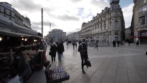 Tiro-De-Carro-En-Cámara-Lenta-Que-Revela-Una-Concurrida-Plaza-Del-Centro-De-Montpellier-Desde-Debajo-De-Un-Mercado-Callejero