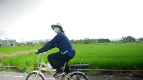 Mujer-Asiática-Vestida-Con-Un-Traje-Azul-Largo-Para-Dormir-Y-Con-Una-Máscara-Facial-Paseando-Por-Exuberantes-Campos-De-Arroz-Verdes