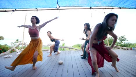 Group-of-Asian-woman-performing-ecstatic-dance-in-circular-formation-on-wooden-deck,-filmed-as-stationary-shot-with-wide-angle-frame