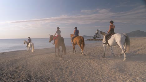 Gruppe-Junger-Frauen,-Die-Am-Strand-In-Richtung-Meer-Reiten-Und-Die-Goldene-Stunde-Des-Sonnenuntergangs-Genießen