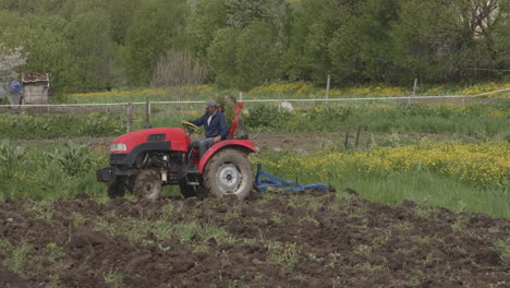 Granjero-Conduciendo-Un-Tractor-Rojo-Arando-Un-Campo-Agrícola-En-La-Aldea-De-Moliti,-Georgia