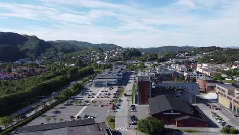 Aufsteigende-Antenne-Vom-Asane-Viertel-Außerhalb-Von-Bergen-Während-Des-Sommermorgens---Sporthalle-Und-Kirche-Neben-Einkaufszentrum-Und-Straße,-Bevor-Die-Ferne-Berglandschaft-Sichtbar-Wird