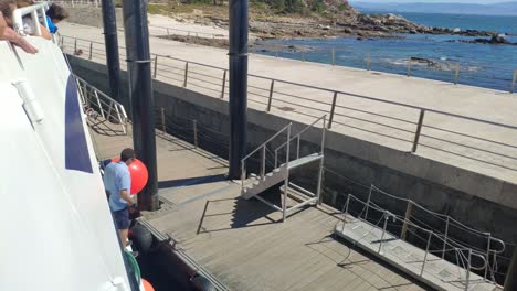 sailors-working-on-the-arrival-of-the-tourist-boat-mooring-the-boat-at-the-jetty-of-the-Cíes-Islands,-sunny-day-in-the-Rías-Baixas,-shot-blocked-down-rolling-to-the-right,-Pontevedra,-Galicia,-Spain