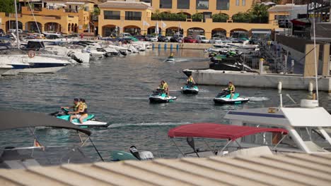 Gruppe-Von-Menschen-Auf-Jetskis,-Die-In-Der-Von-Yachten-Umgebenen-Marina-Vorbeifahren