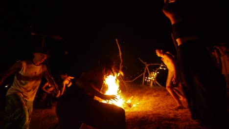 Group-of-Asian-dancers-rotating-around-flaming-hot-ceremonial-fire-during-night-time-dance-performance,-filmed-hand-held-as-wide-shot