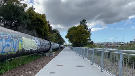 Sendero-Peatonal-De-Hormigón-Con-Valla-Y-Tubería-Grande-Con-Graffiti-De-Pintura-En-Aerosol-único