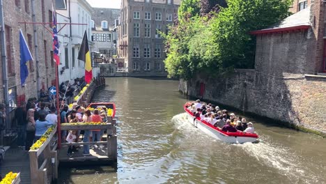 Lancha-Rápida-Con-Pasajeros-Que-Cruzan-El-Canal-De-La-Ciudad-Pasando-Por-Turistas-Que-Esperan-En-La-Terminal-En-Brujas,-Bélgica