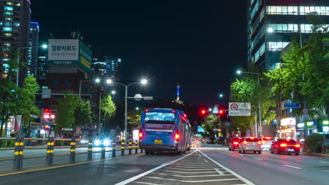 N-Vista-De-La-Torre-Namsan-De-Seúl-Desde-La-Ajetreada-Calle-Del-Centro-De-La-Ciudad-De-Seúl-Por-La-Noche-Con-Un-Lapso-De-Tiempo-De-Tráfico-En-Movimiento-Rápido-Que-Cambia-Los-Semáforos,-Senderos-De-Luz-De-Neón---Movimiento-Panorámico