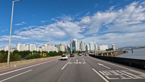 FPV-Drone-flying-along-Gangbyeonbuk-ro-expressway-following-cars-traffic-against-city-skyline-in-Seoul-South-Korea