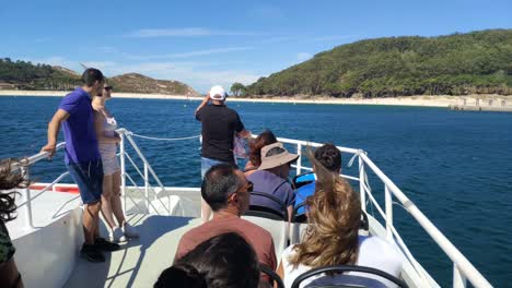 tourists-shooting-photographs-on-the-deck-of-the-boat-arriving-at-the-beach-and-jetty-of-the-Cíes-Islands,-Rías-Baixas,-sunny-day,-rolling-shot-on-the-right,-Pontevedra,-Galicia,-Spain