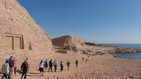 Establishing-shot,-group-of-tourists-walking-outside-of-Abu-Simbel-Temple-complex,-Egypt