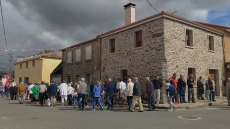 Religiosos-Católicos-Salen-De-La-Iglesia-En-Procesión-Delnado-De-Una-Casa-De-Piedra-En-Celebración-Bajo-El-Control-De-La-Policía,-Día-Nublado,-Tiro-Bloqueado,-Poulo,-A-Coruña,-Galicia,-España