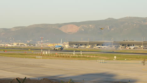 Small-KLM-airplane-lands-at-Barcelona-Airport-at-sunrise,-tracking-shot,-pan