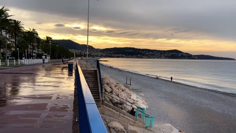 Leute,-Die-Nach-Dem-Regen-In-Der-Dämmerung-In-Nizza,-Frankreich,-An-Der-Promenade-Des-Anglais-Am-Strand-Entlang-Laufen