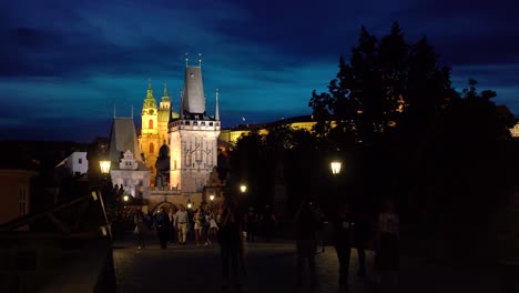 Foto-Nocturna-Del-Puente-De-Carlos-En-Praga-Con-Turistas,-Mirando-La-Torre-Del-Puente-De-Mala-Strana