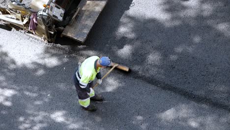 Road-paving-machine-is-laying-the-asphalt-concrete-and-doing-compaction-while-workers-spread-road-stone-with-a-brush