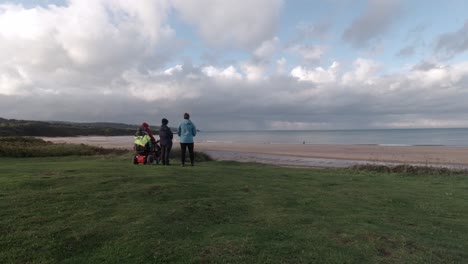 Familia-Que-Apoya-A-La-Abuela-Pensionista-En-Silla-De-Ruedas-Viendo-La-Playa-De-Arena-Nublada