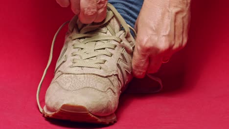 Person-wearing-New-Balance-casual-streetwear-shoes,-then-tying-them-in-a-studio-with-red-background