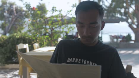 Young-Nepali-Man-looking-at-menu-dining-outdoor-Greece-restaurant