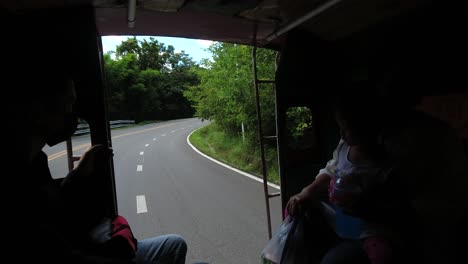 People-riding-back-of-typical-Thai-Songthaew,-looking-out-on-road-behind